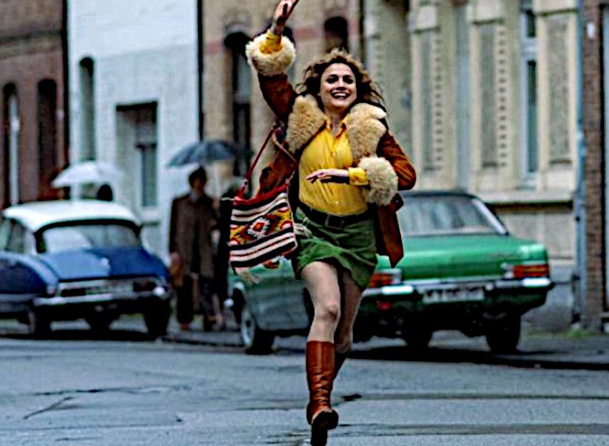 Frau in 70er-Jahre-Kleidung läuft fröhlich auf einer Straße in Köln.