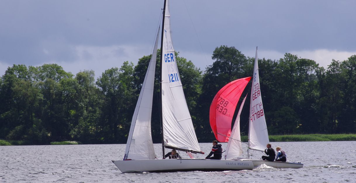 Zwei Segelboote auf einem See bei einer Regatta, umgeben von Bäumen.