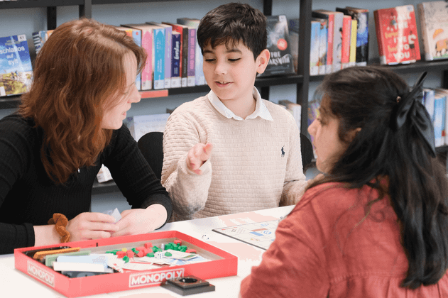 Drei Personen spielen ein Brettspiel in einer Bibliothek.