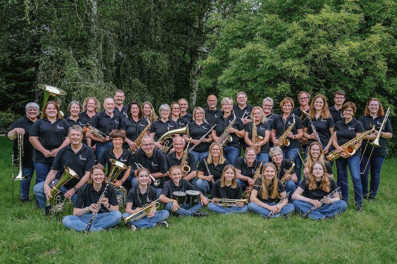 Eine Gruppe von Menschen in schwarzer Kleidung posiert mit Blasinstrumenten auf einer Wiese.