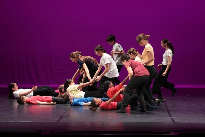 Eine Gruppe von Schülern führt eine Tanzperformance auf einer Bühne mit violettem Hintergrund auf.