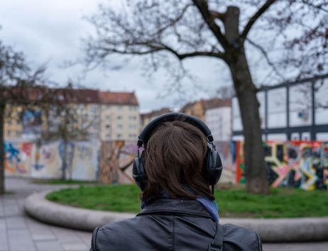 Person mit Kopfhörern steht vor einer mit Graffiti bedeckten Wand in einem urbanen Park.