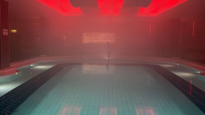 Ein Hallenbad mit roter Beleuchtung und Nebel, der eine unheimliche Atmosphäre schafft.