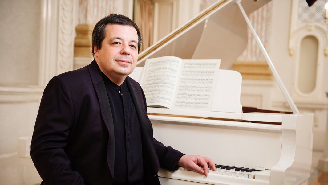 Ein Mann sitzt an einem weißen Flügel mit geöffnetem Notenblatt.