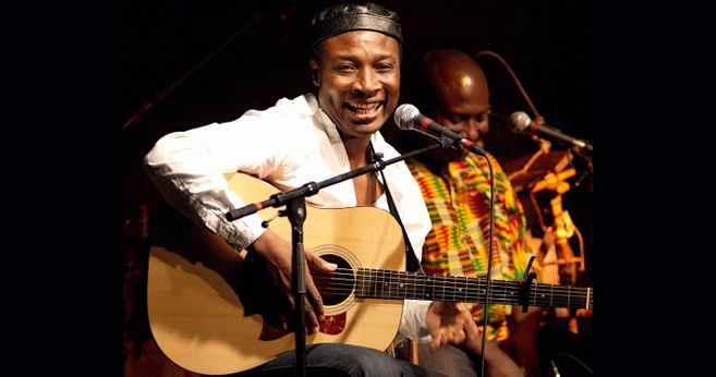 Musiker spielt Gitarre und singt auf der Bühne.