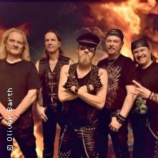 Fünf Männer in Rocker-Outfits posieren vor einem feurigen Hintergrund.