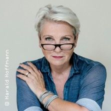 Frau mit kurzen grauen Haaren und Brille, trägt ein blaues Hemd.