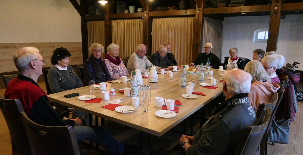 Eine Gruppe älterer Menschen sitzt um einen Tisch in einem Raum mit Holzbalken.