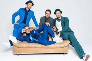 Vier Männer in bunten Anzügen posieren auf einem Sofa.