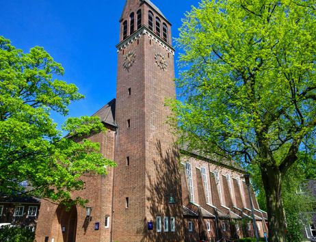Backsteinkirche mit Turm und grünen Bäumen im Vordergrund.