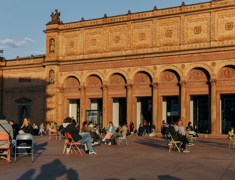 Menschen sitzen auf bunten Stühlen vor der Fassade der Hamburger Kunsthalle im warmen Abendlicht.