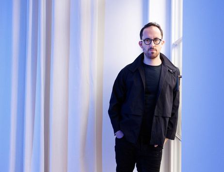Eine Person in schwarzer Kleidung steht vor einem blauen Hintergrund.