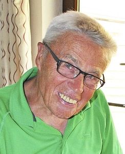 Ein älterer Mann mit Brille und grünem Hemd lächelt in die Kamera.