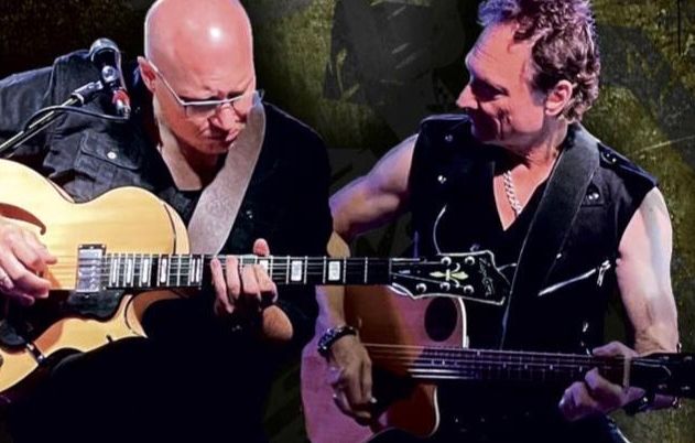 Zwei Männer spielen Gitarren auf einer Bühne.