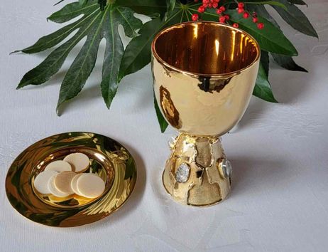 Goldener Kelch und Hostien auf einem Tisch mit grünen Blättern und roten Beeren.