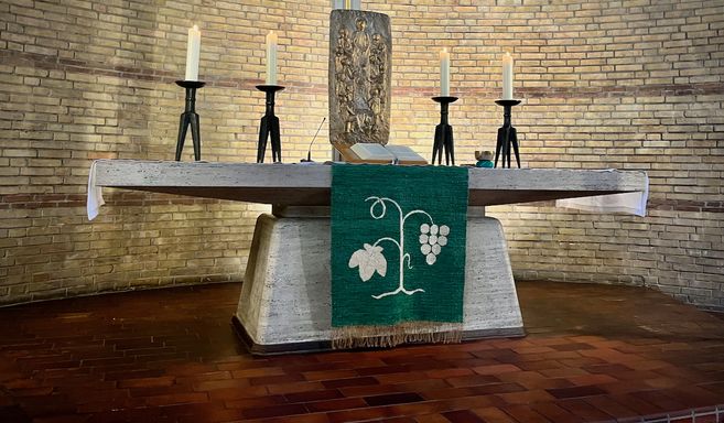 Altar in der Paul-Gerhardt-Kirche mit Kerzen und einem grünen Tuch mit Weinrebenmotiv.