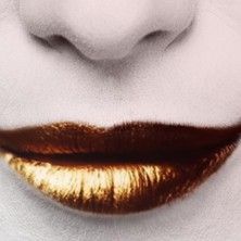 Nahaufnahme von goldfarbenen Lippen auf einem schwarz-weißen Gesicht.