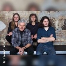 Vier Männer sitzen vor einer alten Backsteinwand.