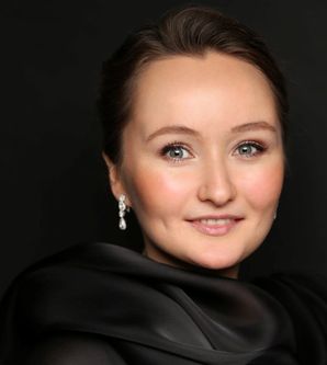 Porträt einer lächelnden Frau mit Ohrringen vor schwarzem Hintergrund.