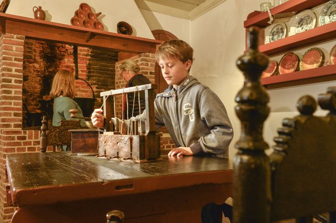 Ein Junge spielt mit einem alten Spielzeug in einem historischen Raum mit Kamin und antikem Geschirr.