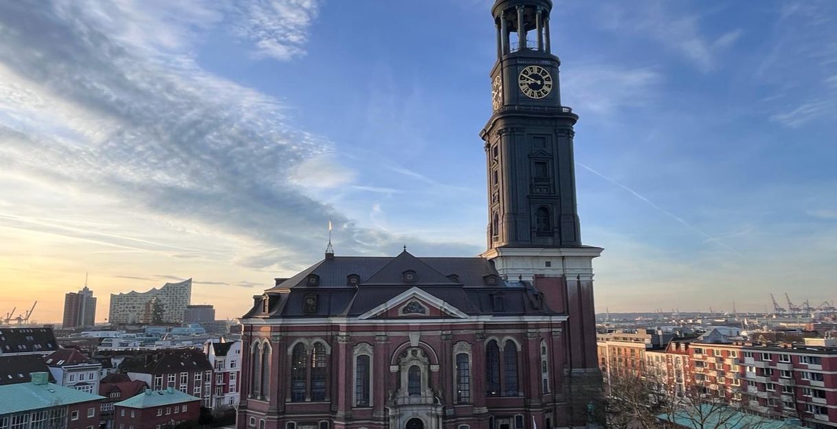 Die Kirche St. Michaelis in Hamburg bei Sonnenuntergang, mit der Elbphilharmonie im Hintergrund.