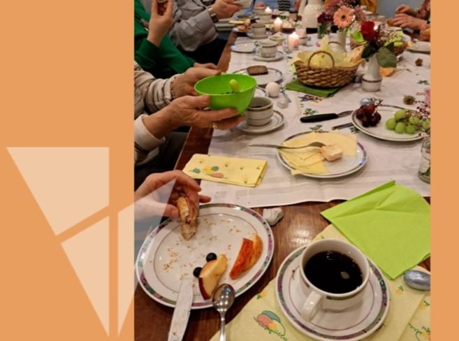 Menschen sitzen an einem gedeckten Frühstückstisch mit Kaffee, Obst und Gebäck.