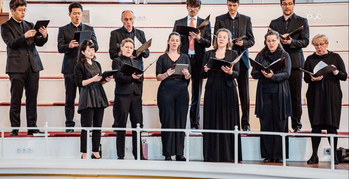 Eine Gruppe von Sängern in schwarzer Kleidung singt auf einer Bühne.