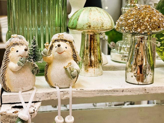 Zwei dekorative Igel mit Weihnachtsmützen und Geschenken, umgeben von glitzernden Pilzen und grünen Glasvasen.