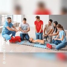 Eine Gruppe von Menschen übt Erste-Hilfe-Maßnahmen an einer Puppe auf dem Boden.