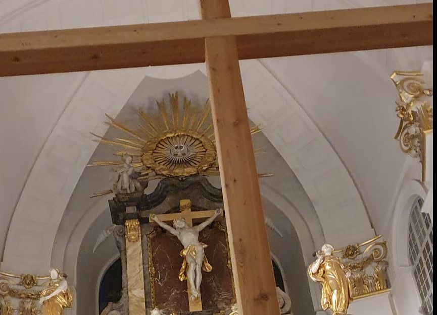 Innenansicht der St. Michaelis Kirche mit einem großen Holzkreuz im Vordergrund und einem kunstvollen Altar im Hintergrund.