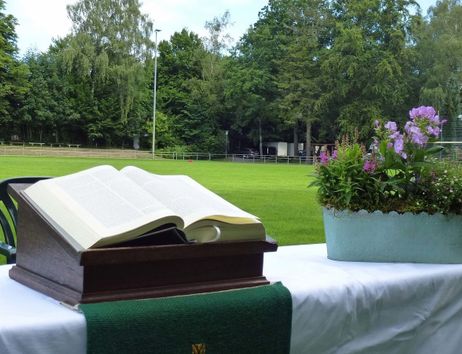 Ein Altar mit einer offenen Bibel und Blumenschmuck auf einem Tisch, der auf einem Fußballfeld steht.