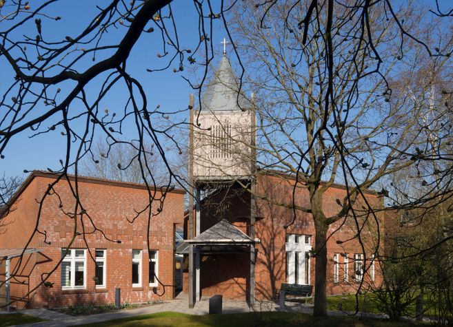 Backsteinkirche mit Glockenturm und Bäumen im Vordergrund.