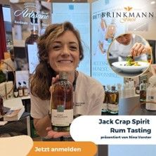 Eine Frau hält eine Flasche Rum auf einer Messe. Im Hintergrund sind Banner und ein Bild von einem Gericht zu sehen.