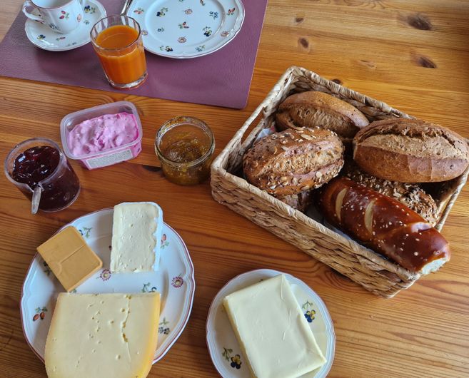Frühstückstisch mit Brötchen, Käse, Marmelade und Getränken.