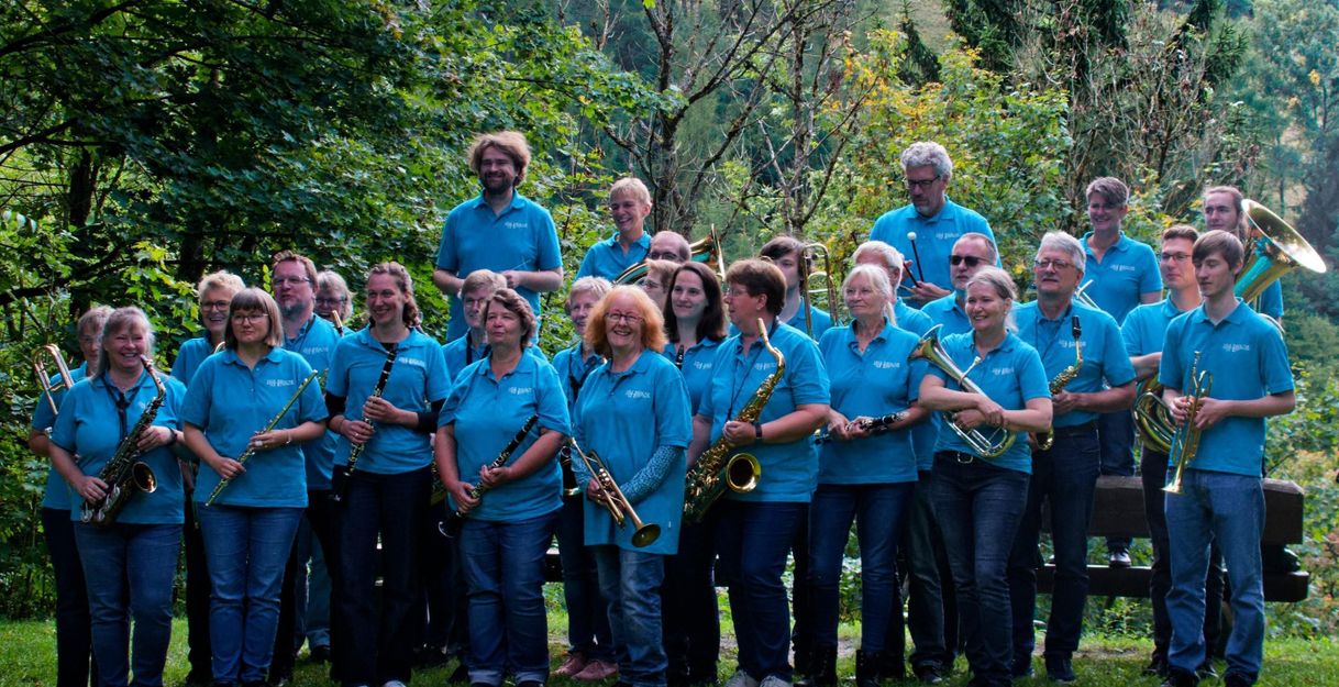 Eine Gruppe von Musikern in blauen Hemden steht im Freien mit Blasinstrumenten.