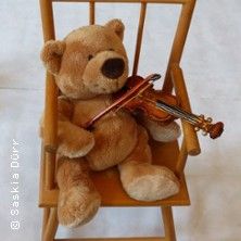 Ein Teddybär sitzt auf einem Schaukelstuhl und hält eine kleine Geige.