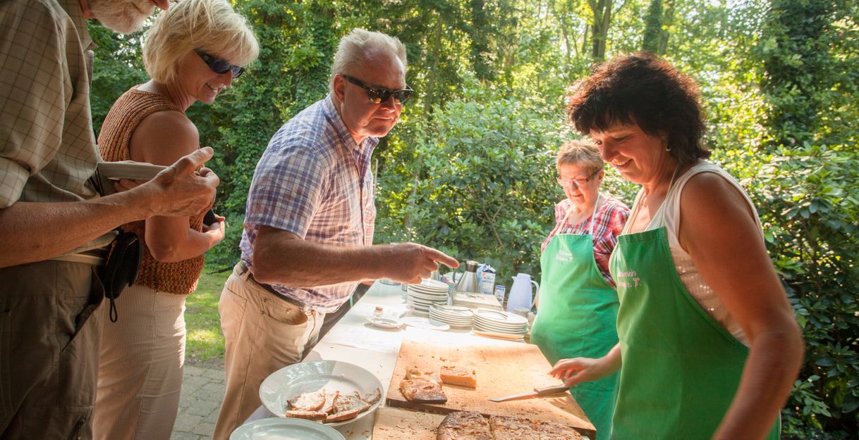 Menschen stehen an einem Tisch im Freien und servieren Butterkuchen.