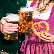 Zwei Personen in traditioneller Tracht halten Bierkrüge und eine Brezel.