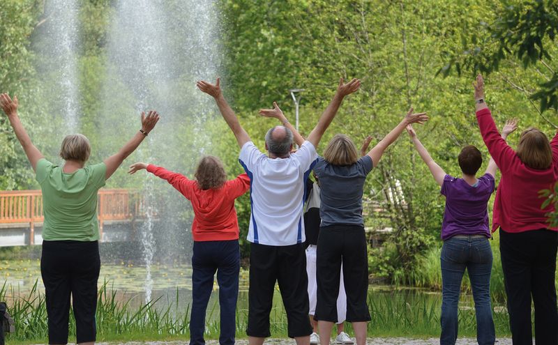 Gruppe von Menschen macht Qigong-Übungen im Freien vor einem Springbrunnen.