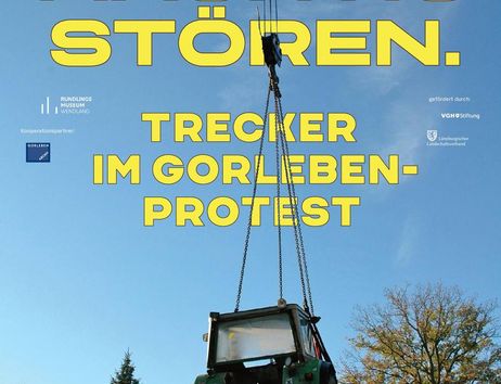 Ein Traktor wird von einem Kran in die Luft gehoben, umgeben von Bäumen und blauem Himmel. Text informiert über eine Ausstellung im Rundlingsmuseum Wendland.