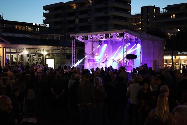 Menschenmenge vor einer beleuchteten Bühne bei einem Abendkonzert im Freien.