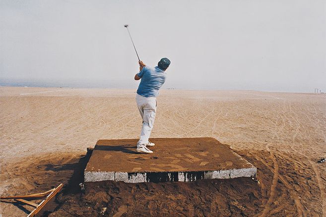 Ein Mann schlägt einen Golfball in einer Wüstenlandschaft.