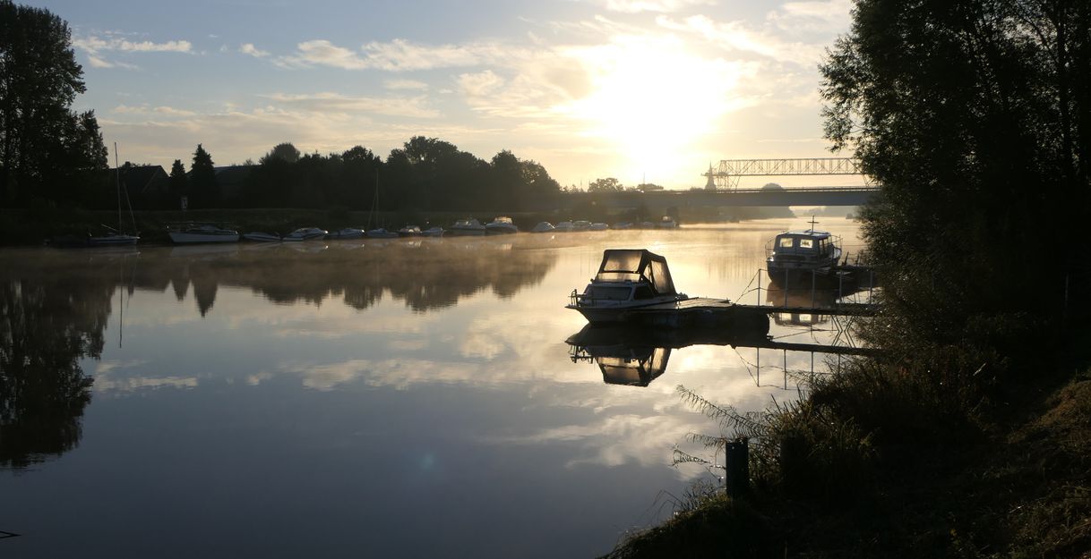 Boote auf einem ruhigen Fluss bei Sonnenaufgang mit Brücke im Hintergrund.