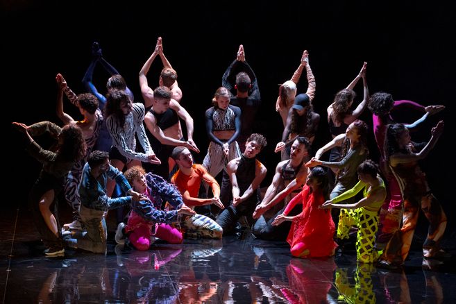 Ausschnitt aus Marco da Silva Ferreiras »A Folia«. Eine Gruppe Tänzer*innen steht in einem Halbkreis mit bunten Kostümen.