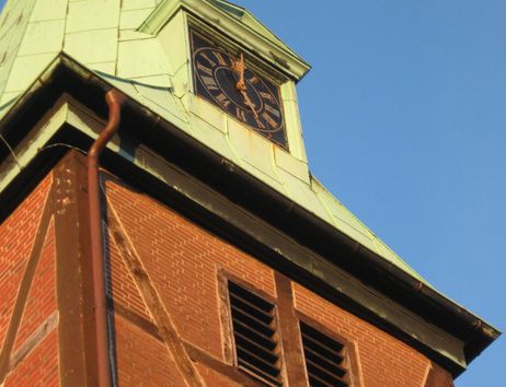 Nahaufnahme eines Kirchturms mit Uhr und grünem Dach vor blauem Himmel.