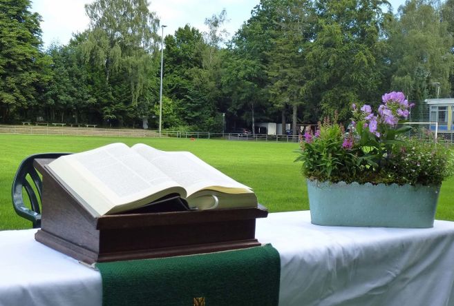 Ein Altar mit einer offenen Bibel und Blumenschmuck auf einem Tisch, der auf einem Fußballfeld steht.