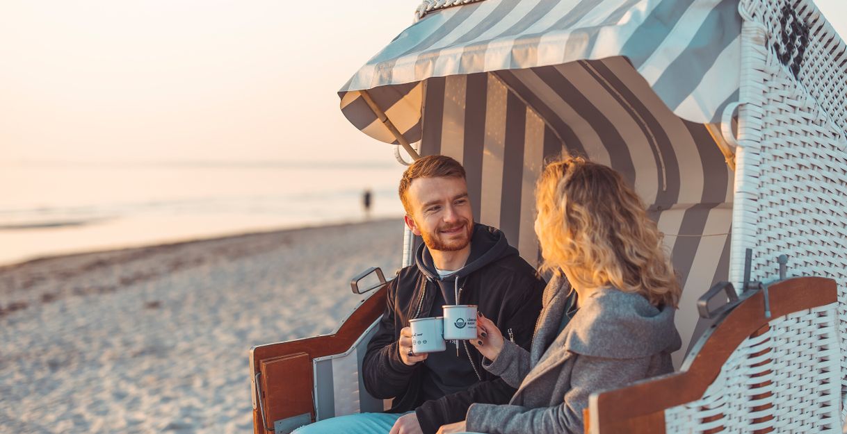 Ein Paar sitzt in einem Strandkorb am Strand und genießt Kaffee bei Sonnenaufgang.