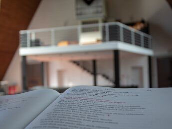 Ein aufgeschlagenes Buch im Vordergrund mit einem modernen Kircheninnenraum im Hintergrund.