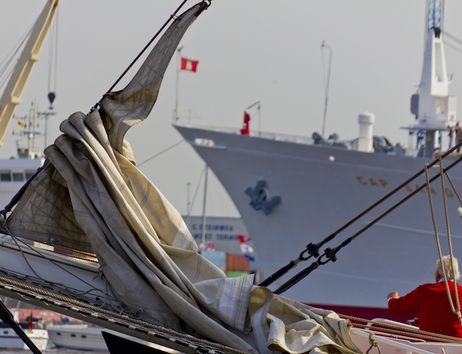 Segelboot mit gefalteten Segeln im Vordergrund, Frachtschiff im Hintergrund im Hamburger Hafen.