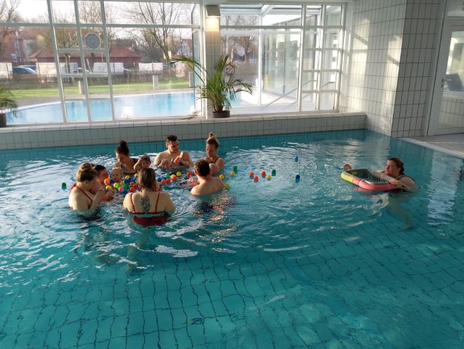Gruppe von Erwachsenen und Babys im Schwimmbad mit bunten Bällen.